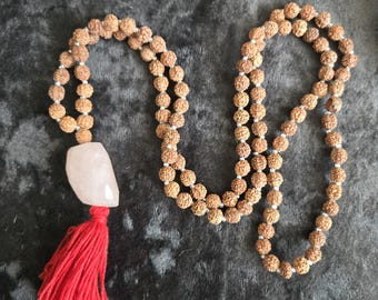 May include: A mala or prayer beads made of brown wood with a pink crystal pendant and a red tassel.