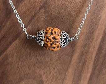 May include: A silver chain necklace with a brown, textured bead. The bead is surrounded by silver accents.