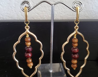 May include: Gold dangle earrings with a geometric design and wooden beads in shades of brown and burgundy.