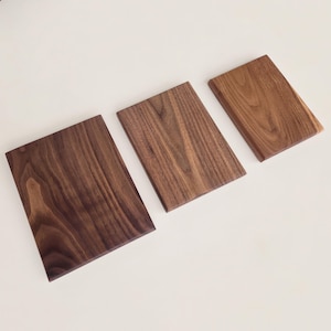 May include: Three rectangular wooden boards arranged in a descending size order from left to right. Each board features a distinct natural wood grain pattern in varying shades of brown, ranging from a deep dark brown to a lighter golden brown tone.