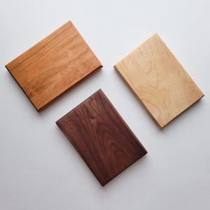 May include: Three rectangular wooden cutting boards in varying shades of brown. The top board is a light reddish-brown, the bottom is a dark brown, and the right board is a light tan color. The boards are arranged on a white surface.