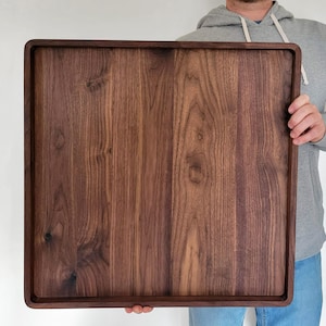 May include: A large, square wooden serving tray with a dark brown finish. The tray has a raised edge and a smooth surface, showcasing the natural wood grain. The tray is approximately 20 inches square.