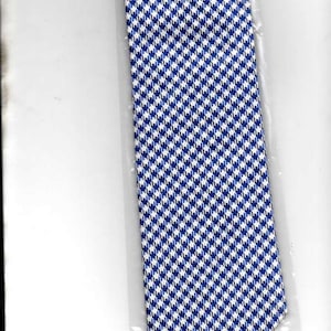 Puede incluir: Una corbata de patrón azul y blanco con un diseño de pata de gallo. La corbata está empaquetada en una bolsa de plástico transparente.