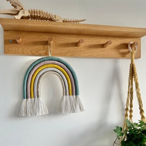 A large rainbow hanging from a peg shelf in a child's bedroom. Made with cotton cord, blue, grey, mustard and gold thread.