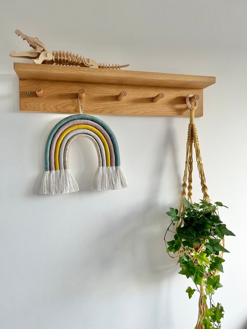 A large rainbow hanging from a peg shelf in a child's bedroom. Made with cotton cord, blue, grey, mustard and gold thread.