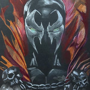 May include: A drawing of the comic book character Spawn, rendered in white and gray on a black background. The character's mask and chest are visible, with a red and orange cape. A chain and skull details are also present.