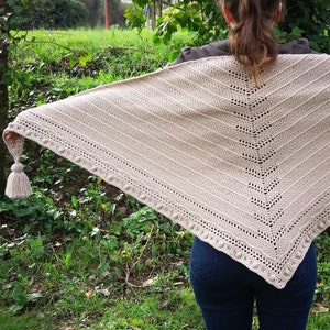 Peut inclure: Un châle en crochet beige avec un pompon. Le châle est drapé sur les épaules d'une personne et est porté à l'extérieur.