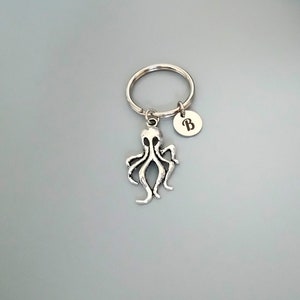 Puede incluir: Llavero de pulpo plateado con un llavero plateado y un dije plateado con la letra "B" grabada.