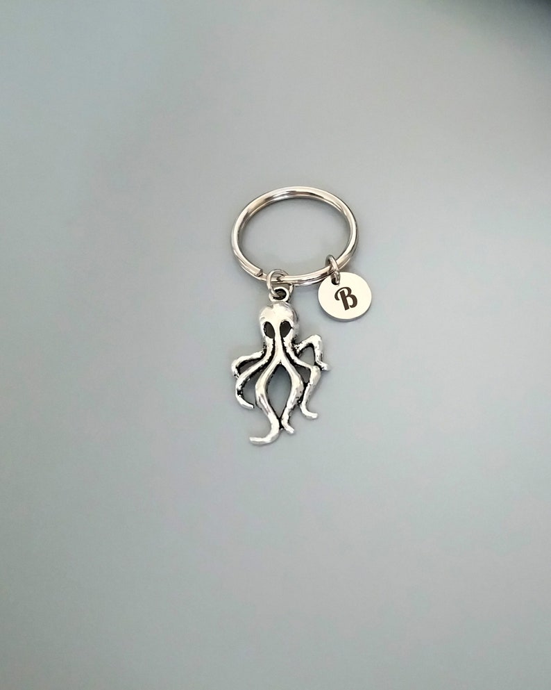 Puede incluir: Llavero de pulpo plateado con un llavero plateado y un dije plateado con la letra "B" grabada.