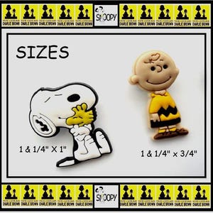 May include: Two cartoon character charms. One is Snoopy, white with black accents and yellow hands, measuring 1 1/4" x 1". The other is Charlie Brown, in a yellow shirt and black zig-zag, measuring 1 1/4" x 3/4". The word "SIZES" is above the charms.
