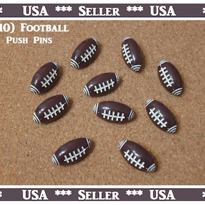 May include: Ten brown football-shaped push pins with white stitching. The push pins are on a brown corkboard. The text (10) FOOTBALL PUSH PINS is printed on the corkboard.