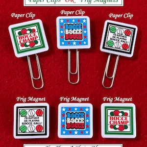 May include: A collection of paper clips and fridge magnets with bocce ball designs. The paper clips and magnets feature square designs with text and graphics in red, white, blue, and green. The text includes "BOCCE CHAMP" and "I'D RATHER BE PLAYING BOCCE BALL!"