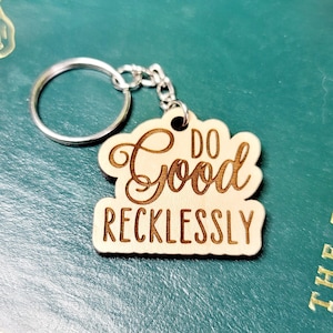 May include: Wooden keychain with a brown background and gold lettering that reads "Do Good Recklessly".