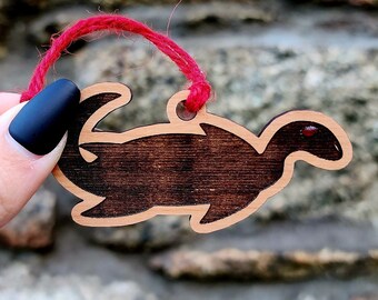 May include: A wooden ornament shaped like a dinosaur, painted brown with a red string attached.