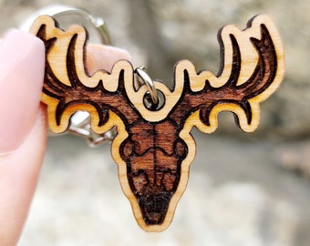 May include: A wooden keychain shaped like a deer skull with antlers. The keychain is brown and has a natural wood finish.