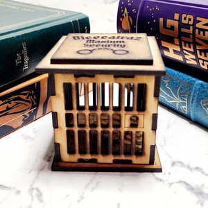 May include: A wooden dice tower with a cage design. The tower is labeled "Dice atraz Maximum Security" and has a pair of glasses icon on the front.