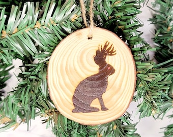 May include: A wooden Christmas ornament with a silhouette of a reindeer with antlers. The ornament is brown and has a natural wood grain.