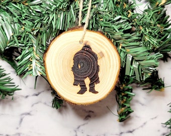 May include: A wooden Christmas ornament with a silhouette of a couple holding hands, hanging from a green pine branch.
