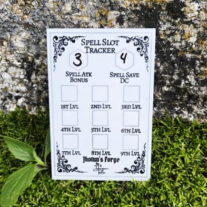 May include: A white rectangular spell slot tracker card with black text and decorative borders. It features fields for Spell Atk Bonus, Spell Save DC, and levels 1st through 9th. The text reads Spell Slot Tracker, Jhotun's Forge, and Dungeon Rose.
