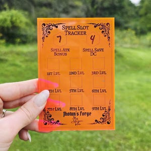 May include: A rectangular orange translucent spell slot tracker with black printed text and decorative filigree corners. The board features sections for spell attack bonus, spell save DC, and levels one through nine, labeled Jhotun's Forge.