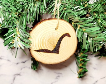 May include: A wooden Christmas ornament shaped like a tree trunk with a black silhouette of a Loch Ness Monster on it.