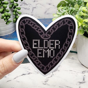 May include: A black heart-shaped sticker with a chain border and the text "ELDER EMO" in white.