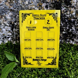 May include: A rectangular yellow acrylic spell slot tracker featuring black printed text and graphics. The board includes sections for Spell Slot Tracker, Spell Atk Bonus, Spell Save DC, and levels 1st through 9th, with the text Jhotun's Forge.