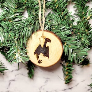 May include: A wooden Christmas ornament with a black silhouette of a mythical creature, possibly a griffin, on a natural wood background.