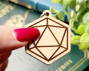 May include: A wooden, light brown, geometric keychain shaped like a twenty-sided die. The keychain is engraved with lines to create a three-dimensional effect.