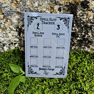 May include: A rectangular white spell slot tracker card featuring black text and decorative borders. The card includes fields for spell attack bonus, spell save DC, and nine levels of spell slots labeled 1st lvl through 9th lvl. The text Jhotun's Forge is printed at the bottom.