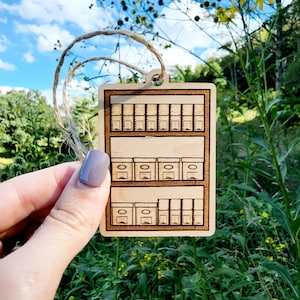 May include: A wooden ornament shaped like a spice rack with three shelves and multiple small square compartments. The ornament is brown and has a rustic look.