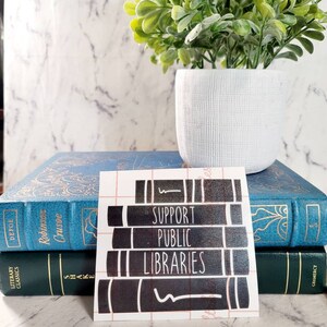 May include: A black and white sticker with the text "Support Public Libraries" on a stack of books. The sticker is on a white background.