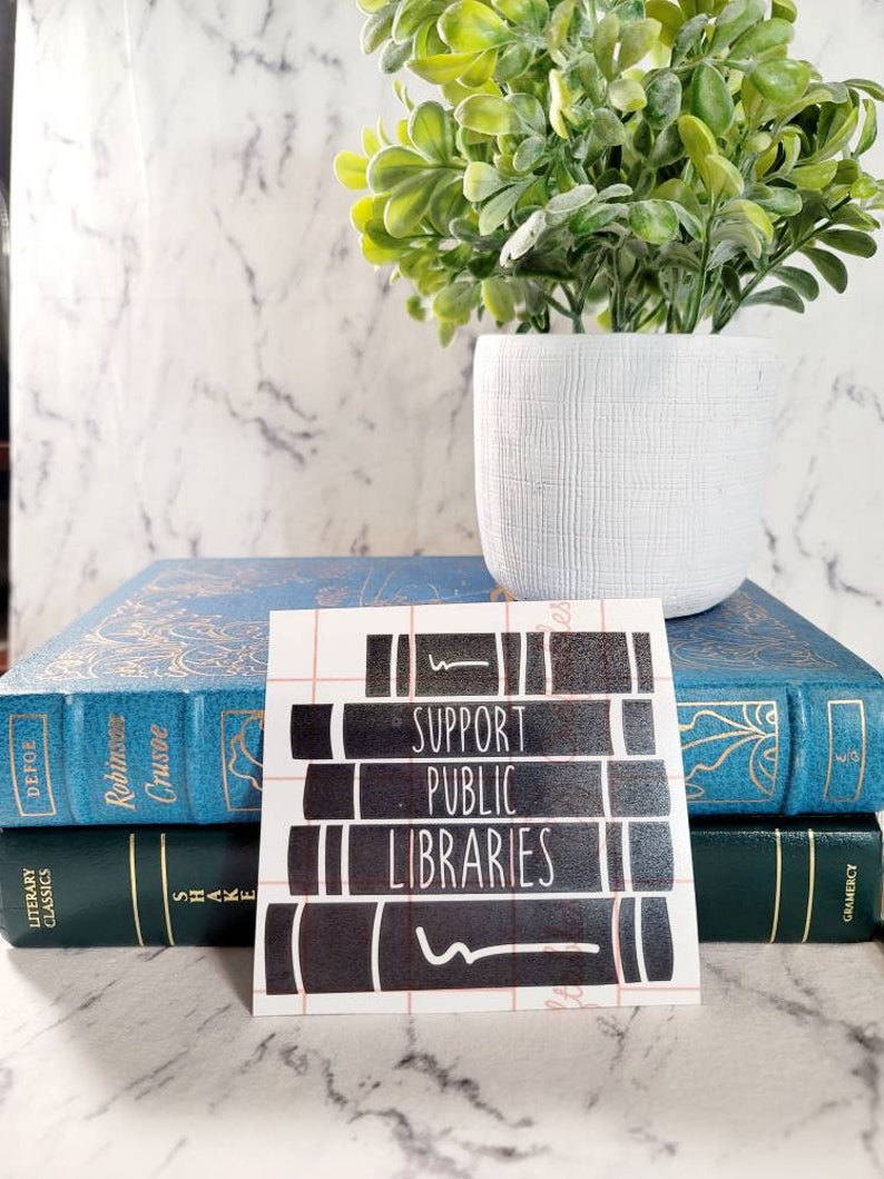 May include: A black and white sticker with the text "Support Public Libraries" on a stack of books. The sticker is on a white background.