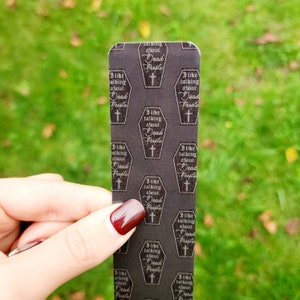 May include: A black and white bookmark with a repeating pattern of a coffin with the text "I like talking about Dead People" inside. The coffin has a cross on top.