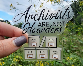 Puede incluir: Una pegatina transparente con el texto "Archivists are not hoarders" en escritura negra. La pegatina presenta una pila de cinco cajas blancas con etiquetas negras y un círculo negro.
