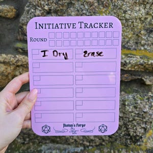 May include: A pink dry-erase initiative tracker with a grid of squares for recording rounds and a space for names. The tracker has a black border and the words "Initiative Tracker" at the top. The bottom of the tracker has a black and white logo with the words "Jhotun's Forge".