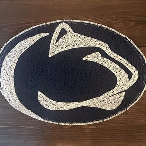 May include: A navy blue and white string art design of a lion's head. The lion's head is outlined in white string and the background is filled in with navy blue string.