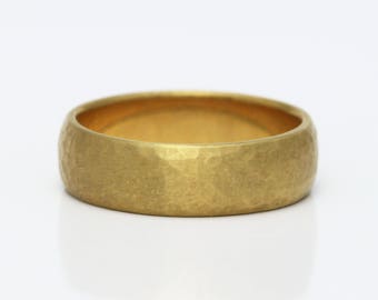 May include: A gold band ring featuring a textured, hammered finish across the outer surface. The ring has a rounded profile and a matte, brushed appearance, showcasing a consistent yellow gold tone throughout the entire circular metal band.