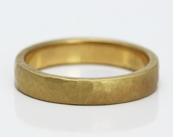 May include: A gold ring with a hammered, textured surface and a matte finish. The band has a consistent width and a rounded interior, showcasing a metallic yellow colour throughout the entire circular structure of the jewellery piece.