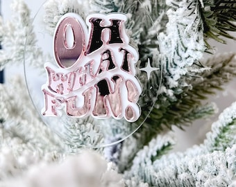 May include: A white and pink acrylic Christmas ornament with the text "Oh What Fun!" in a pink and white font.