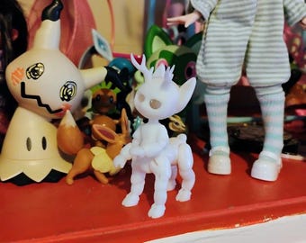 Puede incluir: Una colección de pequeñas figuras, incluyendo una criatura blanca con forma de centauro con cuernos, una figura de Mimikyu y otros personajes de dibujos animados. Una muñeca con un atuendo a rayas se encuentra en el fondo. Las figuras están en una estantería roja.