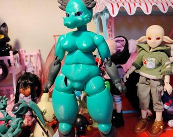 May include: A teal-colored articulated doll with a fox-like head and dark gray accents. The doll has a detailed, stylized design with visible joints and a humanoid form. Other dolls and toys are visible in the background, suggesting a collection or display.