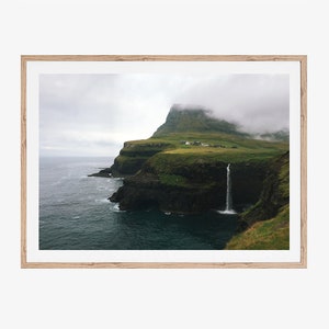 May include: A dramatic landscape photograph of a green, grassy cliff with a waterfall cascading down the side. The cliff is surrounded by a vast, blue ocean and a cloudy sky.