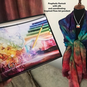 Może przedstawiać: Wydruk w ramie z abstrakcyjnym obrazem kolorowych wir&oacute;w i oł&oacute;wkiem. Wydruk zawiera napis "Create". Jedwabna chusta z wzorem tie-dye w odcieniach niebieskiego, zielonego, pomarańczowego i czerwonego jest prezentowana na manekinie. Chusta jest połączona ze srebrnym naszyjnikiem i wisiorem o dopasowanym abstrakcyjnym wzorze.