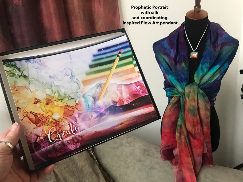 Może przedstawiać: Wydruk w ramie z abstrakcyjnym obrazem kolorowych wir&oacute;w i oł&oacute;wkiem. Wydruk zawiera napis "Create". Jedwabna chusta z wzorem tie-dye w odcieniach niebieskiego, zielonego, pomarańczowego i czerwonego jest prezentowana na manekinie. Chusta jest połączona ze srebrnym naszyjnikiem i wisiorem o dopasowanym abstrakcyjnym wzorze.
