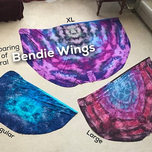 May include: Comparison of three sizes of tie-dye fabric wings, labeled "Regular", "Large", and "XL". The wings are a galaxy print with shades of blue, purple, and pink.
