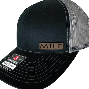 May include: Black and grey trucker hat with a brown leather patch that says "MILF" on the front.