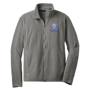 May include: A gray fleece zip-up jacket with a blue embroidered United States Navy logo and the name "ARTHUR" below it.