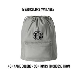 May include: A gray drawstring bag with a front pocket and a black monogram. The text above reads "5 BAG COLORS AVAILABLE." Below the bag, the text reads "40+ NAME COLORS • 30+ FONTS TO CHOOSE FROM."