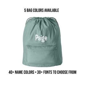 May include: A light green drawstring backpack with a front pocket and the name "Paige" in white. The text above reads "5 BAG COLORS AVAILABLE", and the text below reads "40+ NAME COLORS • 30+ FONTS TO CHOOSE FROM".